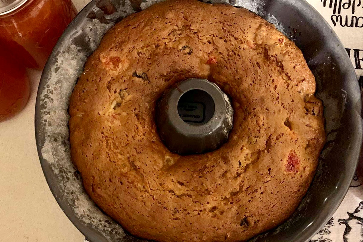 Golden brown cake still in circular Bundt pan, next to two jars of reddish fruit juice.