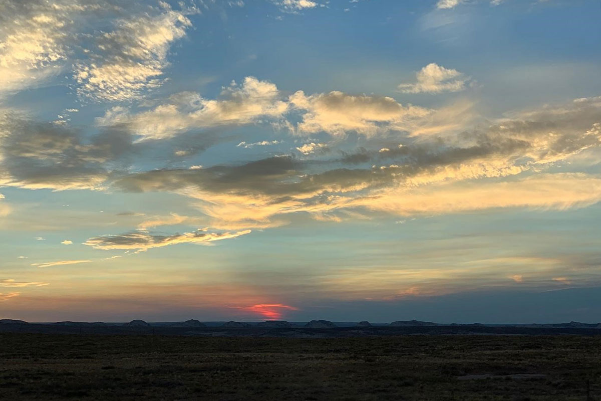 Sunset in the desert, with a red flare of sunshine shining through layers of clouds and haze.