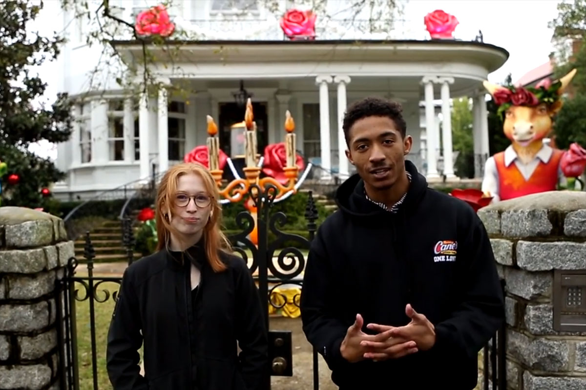 Two young people stand in front of a white house adorned with decorations.