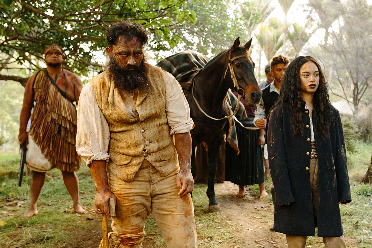 Indigenous people, mostly in dirty colonists' clothing, walk through the woods with a horse. One carries a rifle, and another an axe.