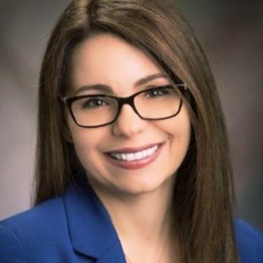 Headshot of a woman with long straight dark hair, glasses, and a blue suit jacket.