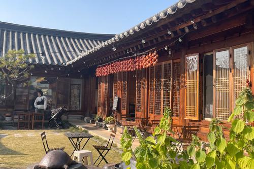 In the courtyard of a wooden home with tiled roof and carved doorways, strings of orange persimmons hang from a bamboo pole hung along an eave. 