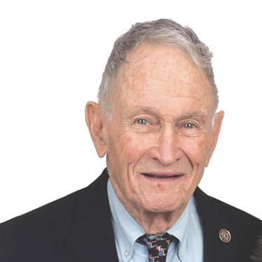 Headshot of a man with short gray hair and a dark jacket with tie.