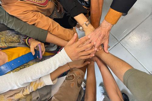 Close-up on many hands outreached into the center of a circle in a sign of teamwork.