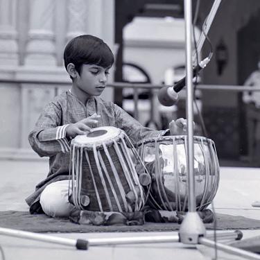 A young boy plays two handdrums on an outdoor stage.