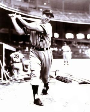 A man swings a baseball bat, in full baseball uniform, in a stadium. Black-and-white photo.