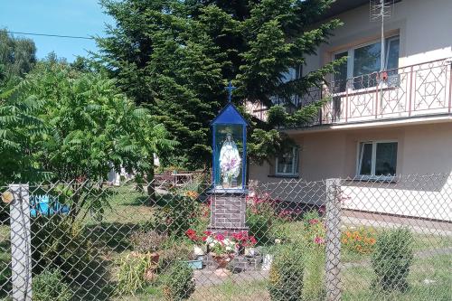 A shrine, about the size of a phone booth, inside a fenced garden, with a female figure in the display.