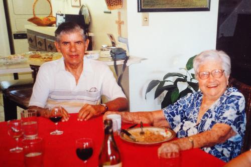 An elder husband and wife, sitting at a dinner table with food and wine.