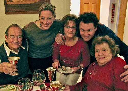 Five adults pose around a table. One man holds up a silver champagne glass, while one woman holds an escargot with a pair of tongs over a plate.