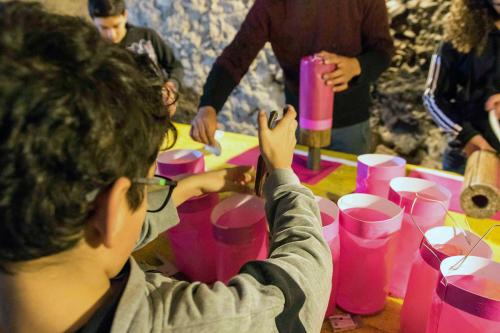 Children and adults at work at a table, shaping cylinders from bright pink paper.