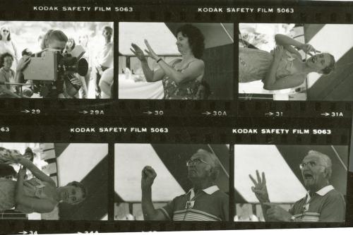 Scan of black-and-white film negative strips. The photos show people speaking using American Sign Language, and a woman filming with a video camera.