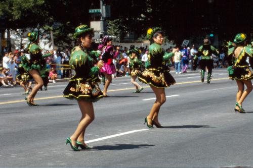 Dancers parade down the street in short green dresses, green hats, and green shoes