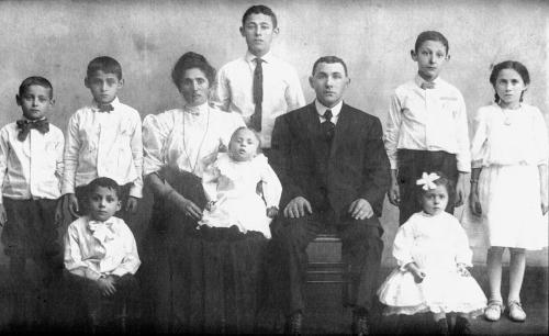 Old black-and-white photo two parents and eight children, the youngest a baby in the mother’s lap.