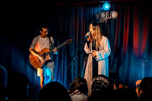 A person playing guitar and another singing on stage before a crowd.