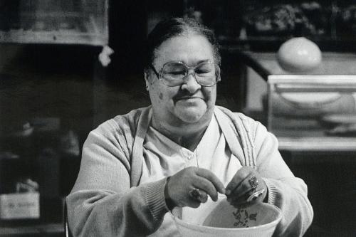 A woman in large glases sits at a kitchen table, working over a porcelain bowl.