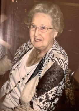 Elder woman with short, curly gray  hair, glasses, and black and white patterned sweater, smiling at the camera.