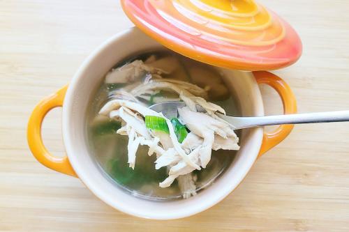 Pot of soup, with a spoon holding up a biteful of shredded chicken.