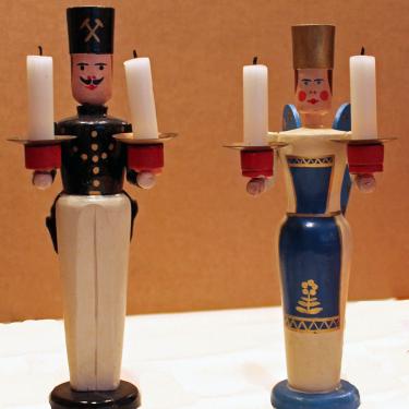 Two wooden candlestick holders in the form of a miner in black and white uniform and an angel in a blue and white robe.
