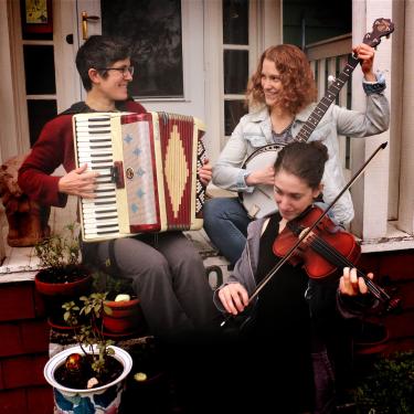 Three-piece band poses on a porch holding their instruments: accordion, banjo, and violin.