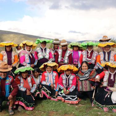 Group of men and women in traditional Andean dress: woven tops, skirts, and hats in bright colors.