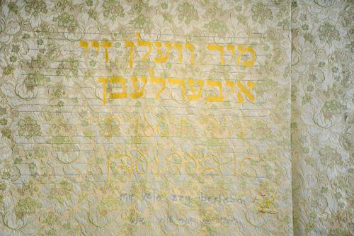 Close-up on the cloth with embroidered Yiddish text in yellow.