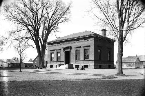 A brick building flanked by two bare trees. Black-and-white photo.