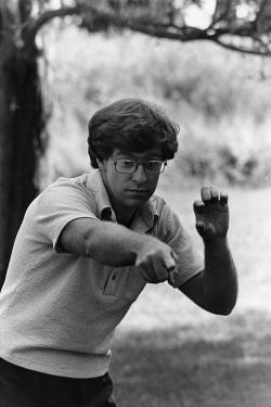 A man gestures, pointing his right hand toward the camera and forming an ASL word with his left.