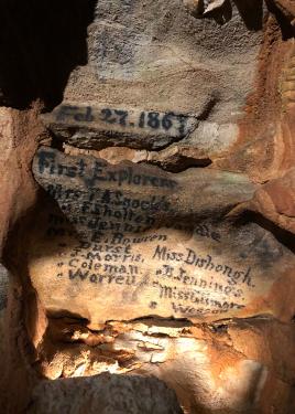 Writing on a wall inside a cave: Feb. 27, 1867. First explorers. With a list of a dozen names that are difficult to read.