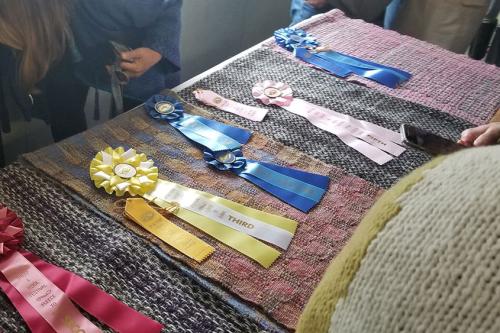 Several woven shawls laid out on a table, with red, yellow, blue, and pink award ribbons.