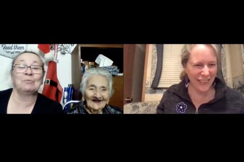 A screenshot of a three-person Zoom call. On the right, an elderly woman and her daughter sit next to each other, in mid-conversation. On the left, a woman looks engaged while listening.