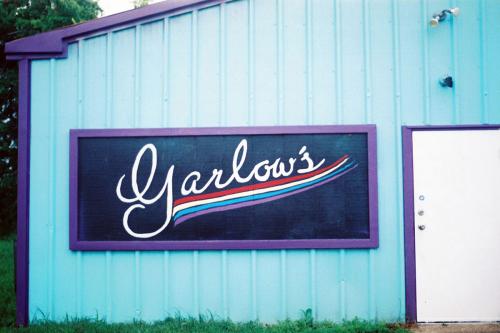 Sign for Garlow’s, written in script and underlined by a rainbow, fixed to the side of a turquoise building with purple trim.