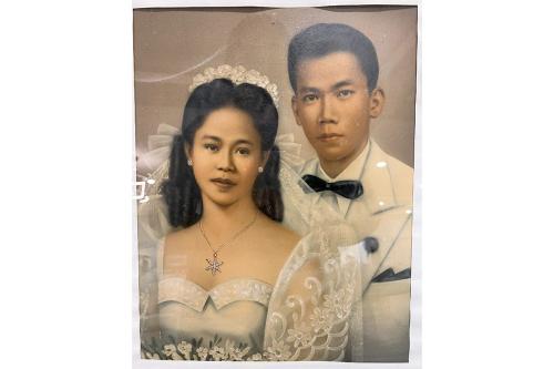 Tinted photograph of a Filipino man and woman in wedding garb. Her white dress includes tall, wide, translucent sleeves.