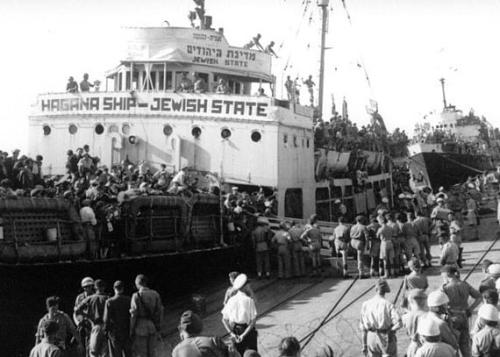 Dozens of people deboard a ship, labeled Hagana Ship - Jewish State. Black-and-white photo.