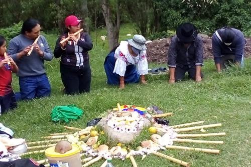 People play flutes and kneel in prayer around an altar.
