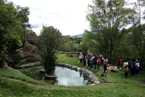 A small group of people gather outdoors around a pond.