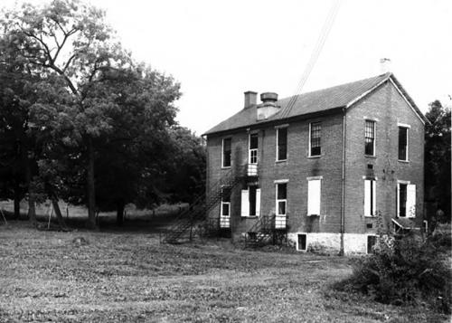 A small two-story brick building among trees and grass. Black-and-white photo