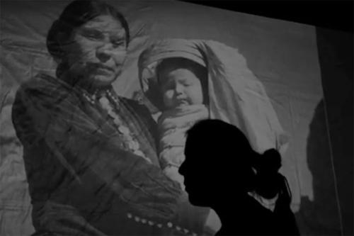 The shadow of someone’s head in profile partially obscures a projection of a black-and-white photograph of a woman holding a small baby.