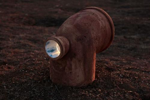 A close up of a ceramic pipe faces away from the photographer. Through a small hole in the back of the pipe, one can glimpse the sky painted on its interior.