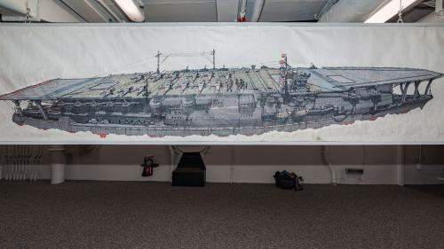 Entirety of an aircraft carrier drawn on paper, hung up and stretching several feet across.