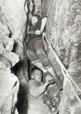 A man and woman descend through a tight crevasse using ropes. Black-and-white photo.