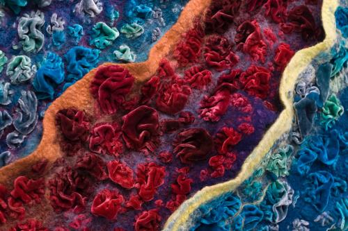 Closeup on textile art, ruffled velvety strips of color arranged like waves on a shoreline.