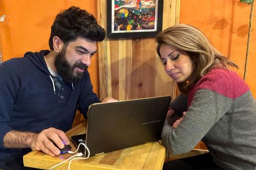 A man and a woman work on a laptop at a small cafe table.