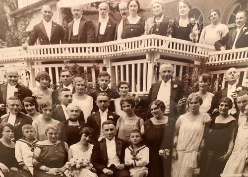 More than thirty people, including adults and children, pose outside a home, wearing fancy suits and dresses. Black-and-white photo.