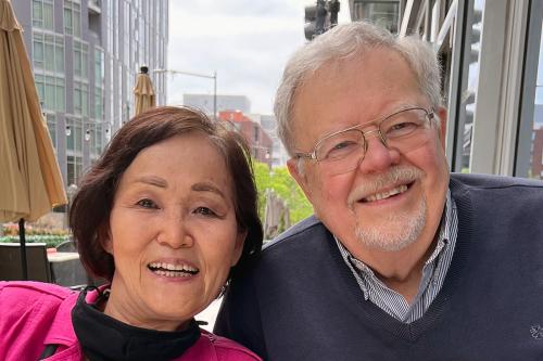 A woman and man pose smiling outdoors in a city.