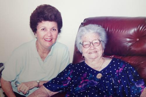 An elder woman and her grown daughter, posing and smiling.