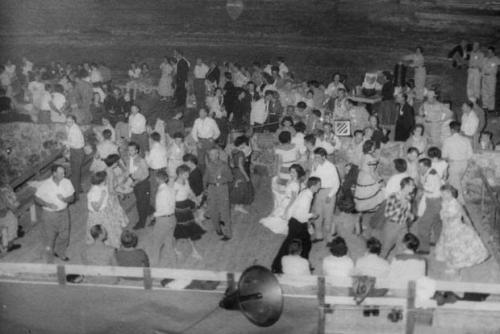 Dozens of people square dancing in a carvern. Black-and-white photo.