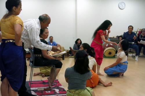 Musicians and dancers rehease. Some are seated on the ground.