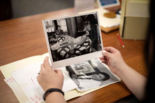Two hands open up a manilla folder containing two black-and-white photos: one a portrait, another three women holding up a handmade blanket.