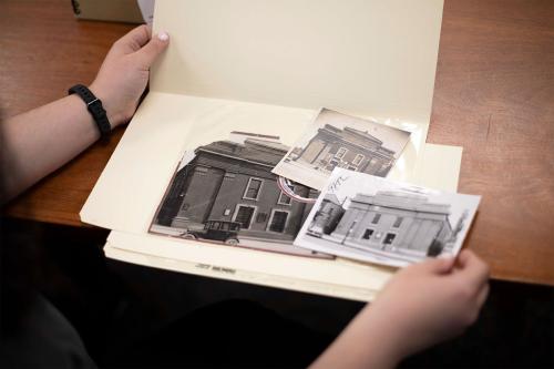 Two hands open up a manilla folder containing black-and-white photos of church buildings.