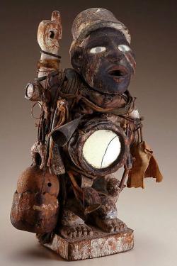 Ceramic or wooden sculpture of a person in a bowler hat, carrying some kind of instrument. Its abdomen appears hollowed out and lit from within.